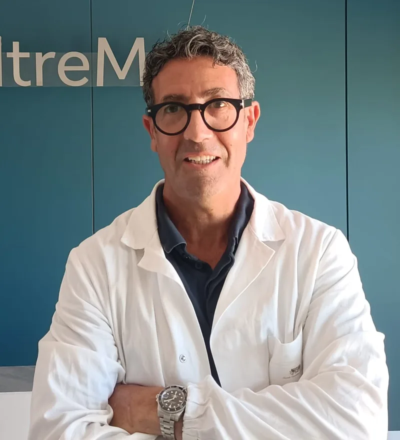 Dott. Daniele Pierucci, in camice bianco, con le braccia incrociate davanti all’insegna OltreMed