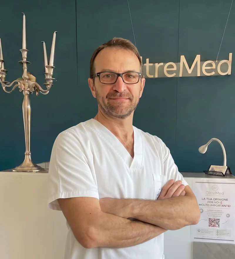Piergiorgio Pirani, in divisa bianca, con gli occhiali e le braccia incrociate davanti all’insegna OltreMed
